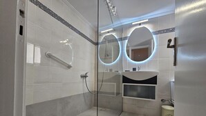 A modern bathroom with a glass shower enclosure, a handrail, a sink with a vanity, and a toilet. - Homely Stay at Acropolis Museum (Athens)