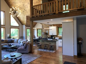 A spacious living area with a high ceiling, wooden beams, a large sofa, a dining table, and a kitchen with white cabinets. - "New Home" Idyllic  Mt Views ,Pond & Horse farm views 2 min to Town (Windham)