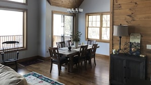 Un comedor con una mesa y sillas de madera, ventanas amplias y una araña.