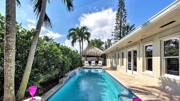 Piscina com espreguiçadeiras e uma estrutura de telhado de palha ao fundo.