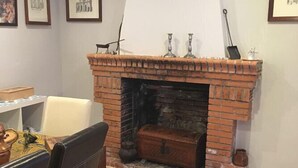 A room with a brick fireplace, a dining table with chairs, and framed pictures on the wall. - Casa Rural Las Violetas (Villanueva de los Infantes)