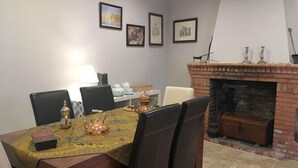 A dining area with a table set for four, a fireplace, and framed artwork on the wall. - Casa Rural Las Violetas (Villanueva de los Infantes)