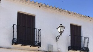 A building with a white facade, a brown door, and two windows with black railings. - Casa Rural Las Violetas (Villanueva de los Infantes)