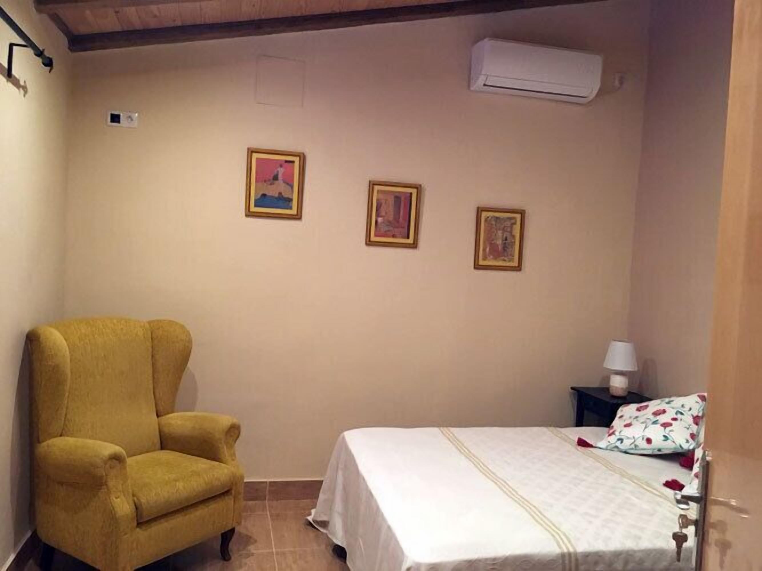 Una habitación con una cama, un sillón amarillo y tres cuadros en la pared.