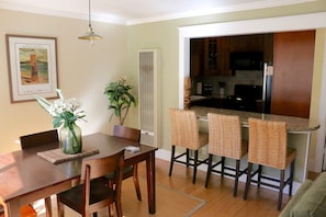 A dining area with a wooden table and chairs, a vase with flowers, and a kitchen with a microwave and bar stools. - Hideaway 1 BR/1 BA One Block from Beach, Snowbirds welcome (Santa Cruz)