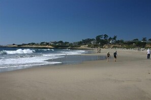 A beach with people walking along the shore, waves crashing onto the sand, and buildings in the background. - Hideaway 1 BR/1 BA One Block from Beach, Snowbirds welcome (Santa Cruz)