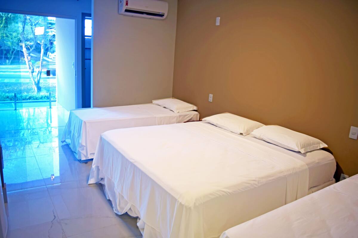 A hotel room with two beds, a large window, and an air conditioning unit.