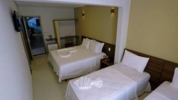 A hotel room with two single beds, a small desk, a chair, a mirror, and a television on the wall.