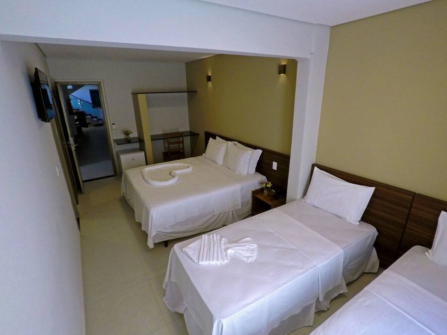A hotel room with two single beds, a small desk, a chair, a mirror, and a television on the wall.