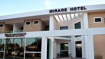A modern hotel with a prominent sign reading "MIRAGE HOTEL" and a restaurant named "MIRAGE RESTAURANTE CHURRASCA SELF-SERVICE" below it.