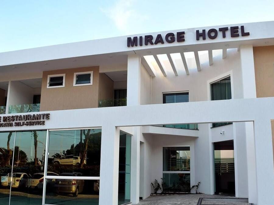 A modern hotel with a prominent sign reading "MIRAGE HOTEL" and a restaurant named "MIRAGE RESTAURANTE CHURRASCA SELF-SERVICE" below it.