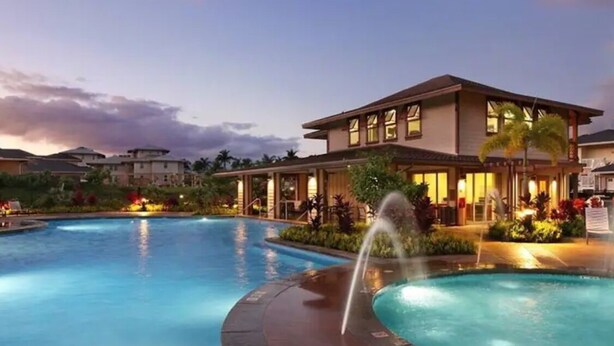 Un hôtel doté d’une piscine, d’une fontaine et d’une façade bien éclairée au crépuscule.