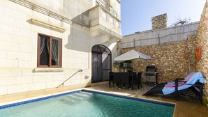 A swimming pool with a stone wall and a patio area with a table and chairs. - Girgentina (Xaghra)