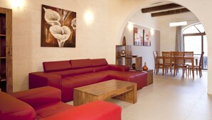 A spacious living area with a red sectional sofa, a wooden coffee table, and a dining area with wooden chairs and a table. - Girgentina (Xaghra)