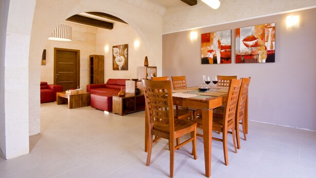 A dining area with a wooden table and chairs, a red sofa, and a painting on the wall. - Girgentina (Xaghra)