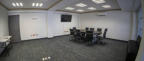 A conference room with a round table, chairs, a TV, and a carpeted floor.