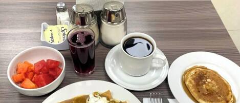 Una mesa de comedor con un plato de enchiladas, huevos revueltos y una taza de café. Se observan salsas y un jarrón con flores al fondo.