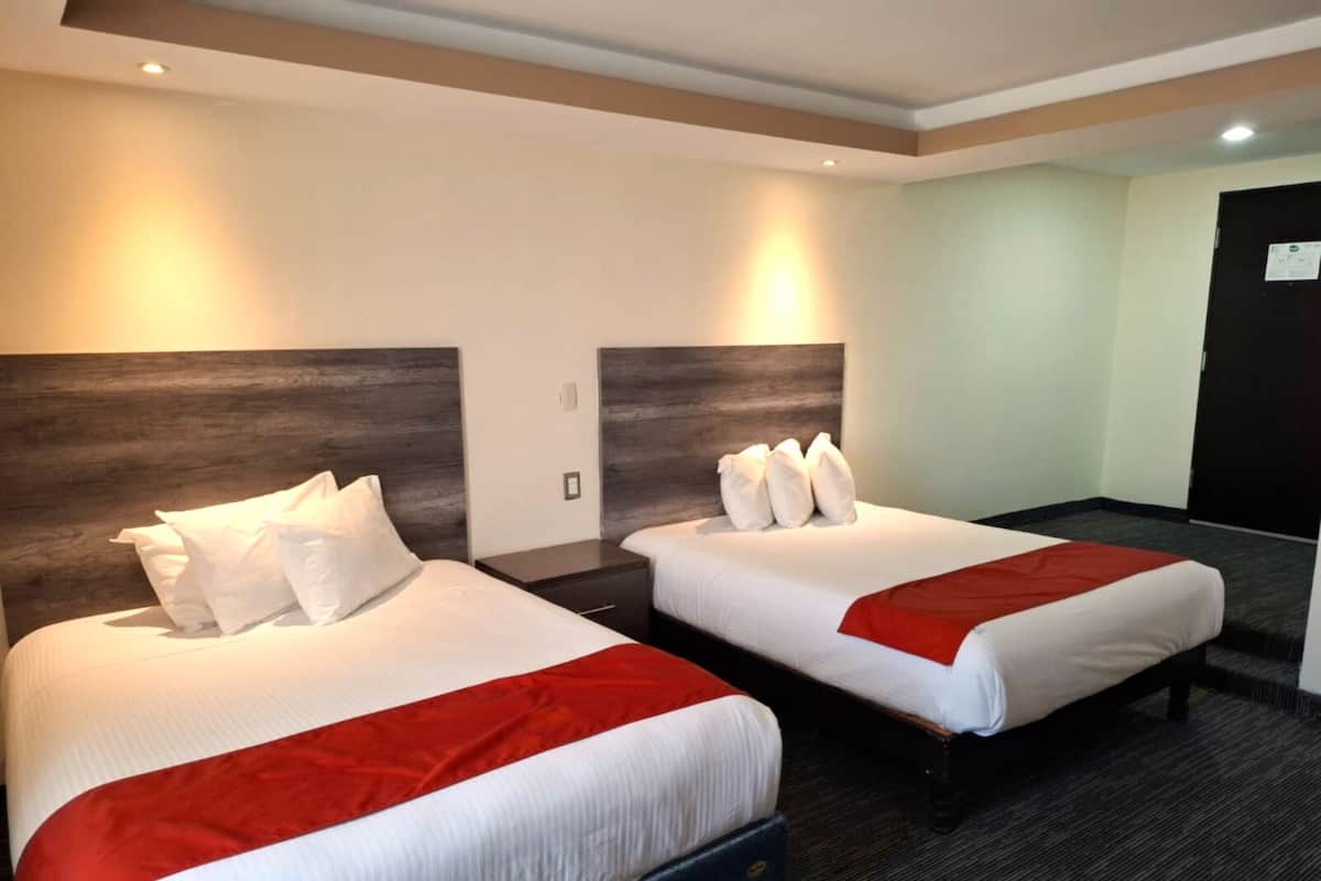 Two double beds with white linens and red accents, wooden headboards, and a carpeted floor in a hotel room.