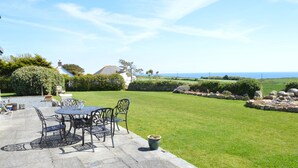 A patio with a table and chairs, a stone pathway, and a view of the sea. - Trendrennen Farm B&B (Penzance)