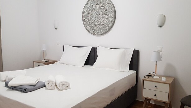 A neatly made bed with white linens and rolled towels, a bedside table with a lamp, and a wall-mounted decorative plate.