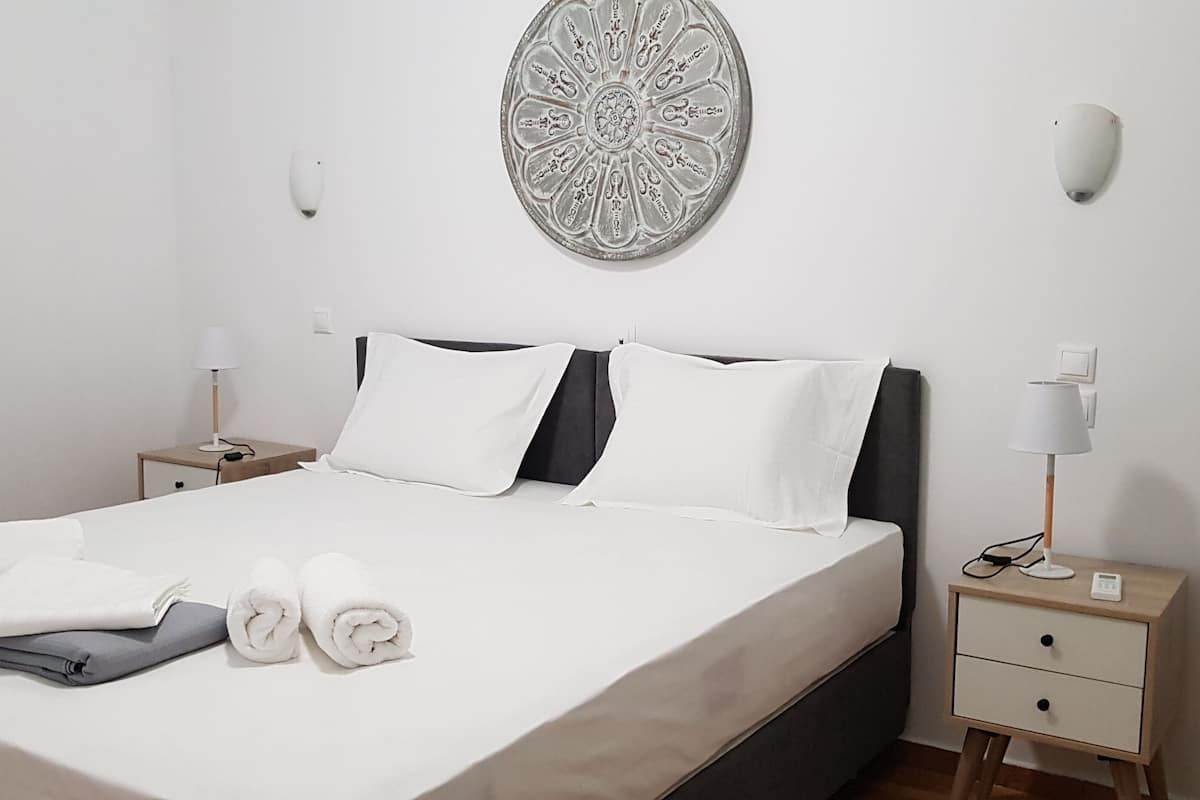 A neatly made bed with white linens and rolled towels, a bedside table with a lamp, and a wall-mounted decorative plate.