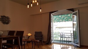 A living room with a sofa, dining table, chairs, a lamp, and a view through a sliding glass door.