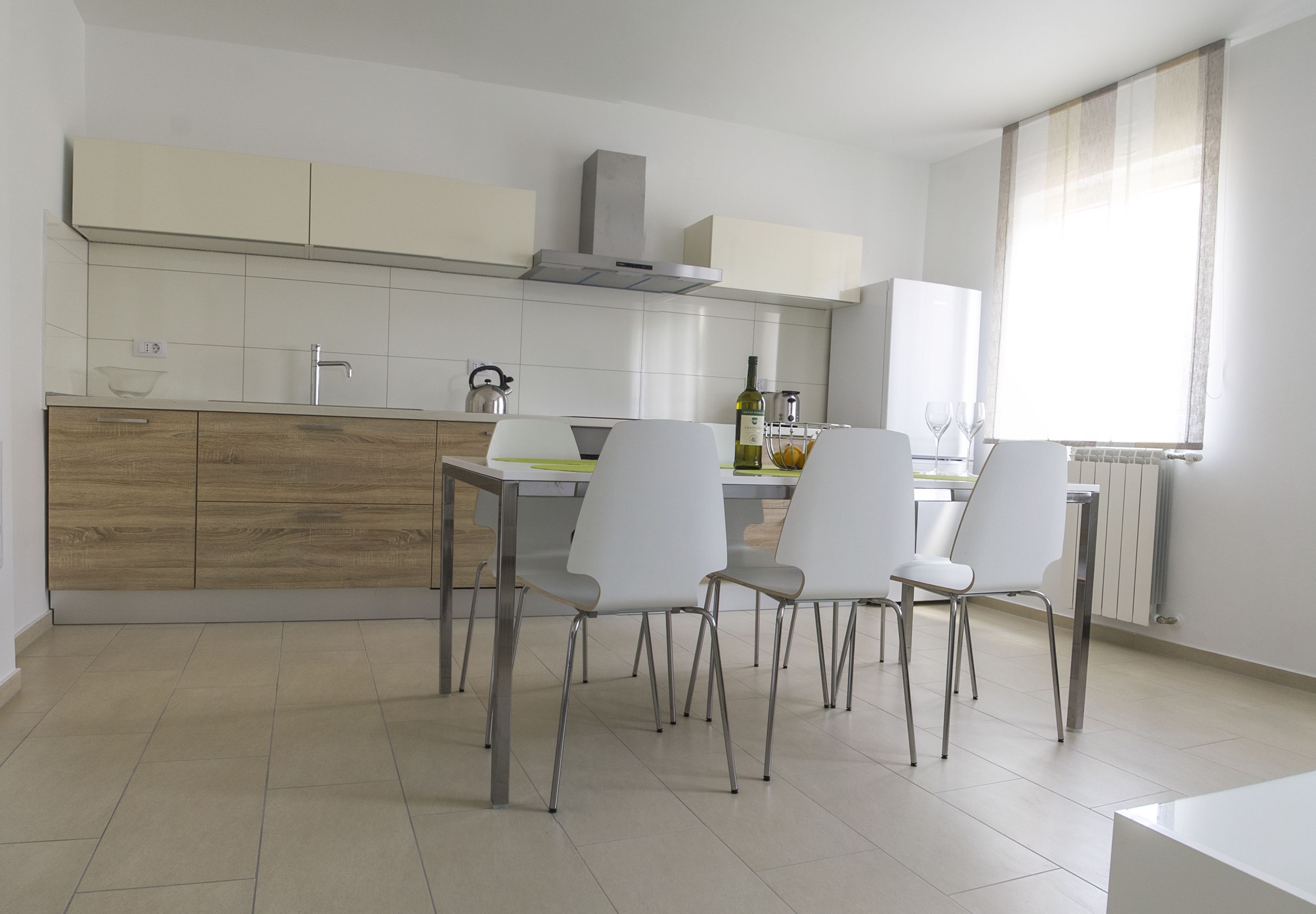 A modern kitchen with white cabinets, a wooden countertop, and a dining area with white chairs.