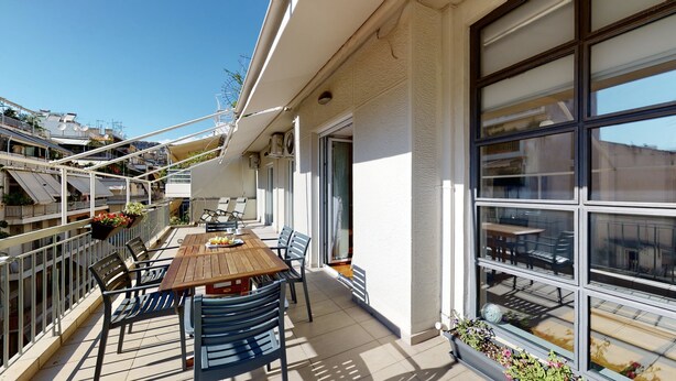 A balcony with a wooden table, chairs, and potted plants. - Penthouse of light at Koukaki (Athens)