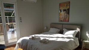 A neatly made bed with rolled towels, a nightstand with a lamp, and a poster on the wall. - Penthouse of light at Koukaki (Athens)