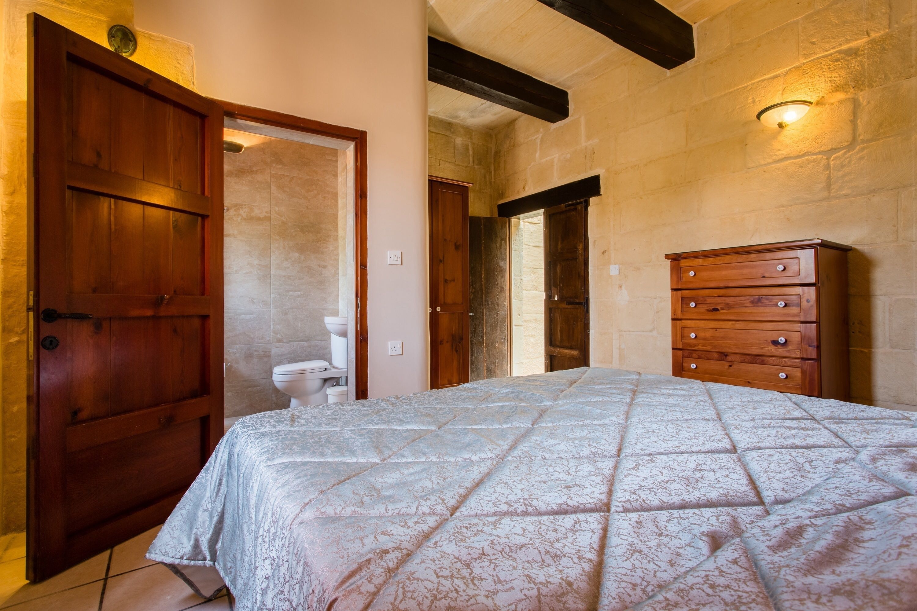 A bedroom with a bed, wooden dresser, and a bathroom visible through an open door.