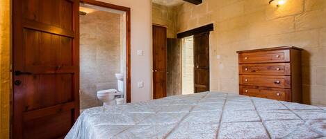 A bedroom with a bed, wooden dresser, and a bathroom visible through an open door.