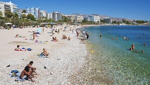 Ein Strand mit badenden und sonnenden Menschen, umgeben von Gebäuden.