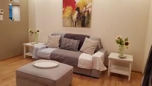 Ein modernes Wohnzimmer mit einer Couch, einem Hocker und zwei Beistelltischen mit Vasen.