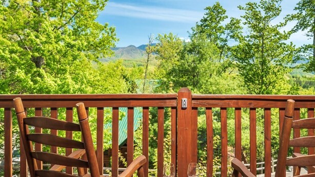 Una terraza de madera con dos sillas y una mesa, con vistas a un paisaje verde y exuberante con árboles y montañas.