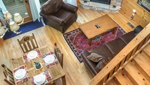 Un acogedor interior de cabaña con chimenea de piedra, sofá de cuero, mesa de comedor y televisor sobre la chimenea.