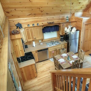 A compact kitchen with wooden cabinets, a refrigerator, a stove, and a dining table set for four. - 1BR Log Cabin w/View, Hot Tub, Pool Table, Arcade, in Black Bear Falls Resort! (Gatlinburg)