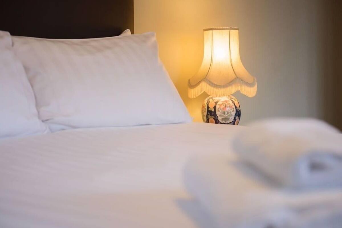 A neatly made bed with white linens and a decorative lamp with a floral pattern.