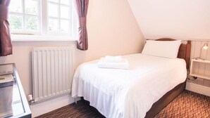 A bedroom with a bed, a radiator, a window with curtains, and a bedside table with a lamp. - The Burley Inn (Ringwood)