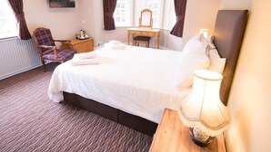 A hotel room with a large bed, a desk, a chair, a TV, and a window with curtains. - The Burley Inn (Ringwood)