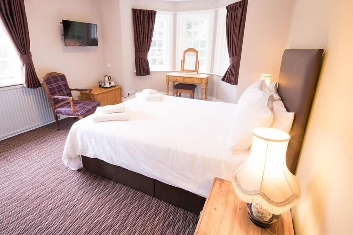 A hotel room with a large bed, a desk, a chair, a TV, and a window with curtains.
