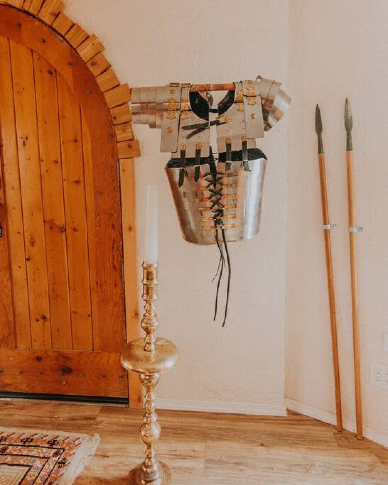 A room with a wooden door, a wall-mounted decorative item resembling a helmet, a candlestick, and two spears.