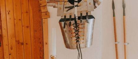A room with a wooden door, a wall-mounted decorative item resembling a helmet, a candlestick, and two spears.