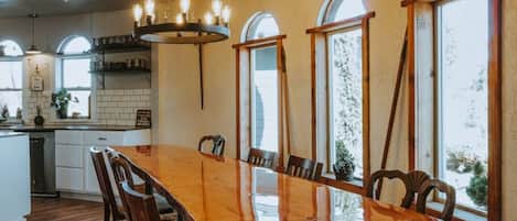 A spacious dining area with a long wooden table, surrounded by chairs, and large windows providing natural light.