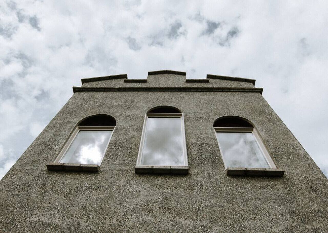 Een hoog, smal gebouw met drie gelijkmatig verdeelde, gebogen ramen in de gevel.