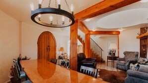 A spacious living room with a large wooden dining table, leather sofas, and a staircase leading to an upper level. - Sequim Lavender Castle (Sequim)