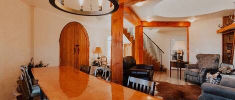 A spacious living room with a large wooden dining table, leather sofas, and a staircase leading to an upper level.
