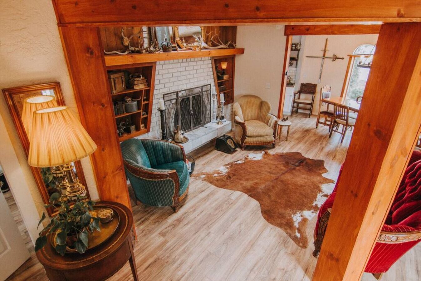 Een gezellige woonkamer met een open haard, een groene fauteuil, een leren vloerkleed en een houten plank met gewei.