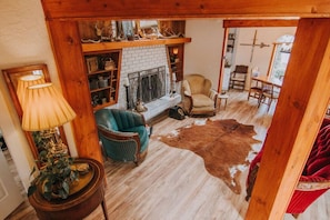 A cozy living room with a fireplace, a green armchair, a leather rug, and a wooden shelf with antlers. - Sequim Lavender Castle (Sequim)
