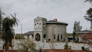 A circular stone building with a tower, arched windows, and a central chimney. - Sequim Lavender Castle (Sequim)