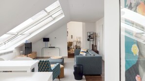 Un appartement moderne de style « loft », doté d’une verrière, d’un espace de vie avec un canapé et une table à manger, et d’une cuisine située à l’arrière-plan.